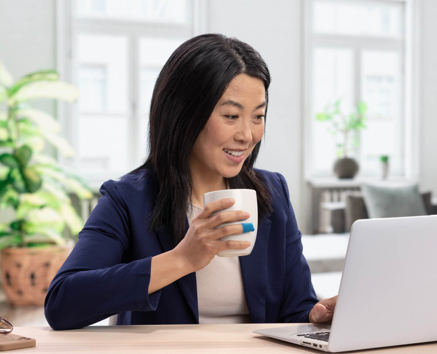 employee smiling, drinking coffee, and working on her laptop